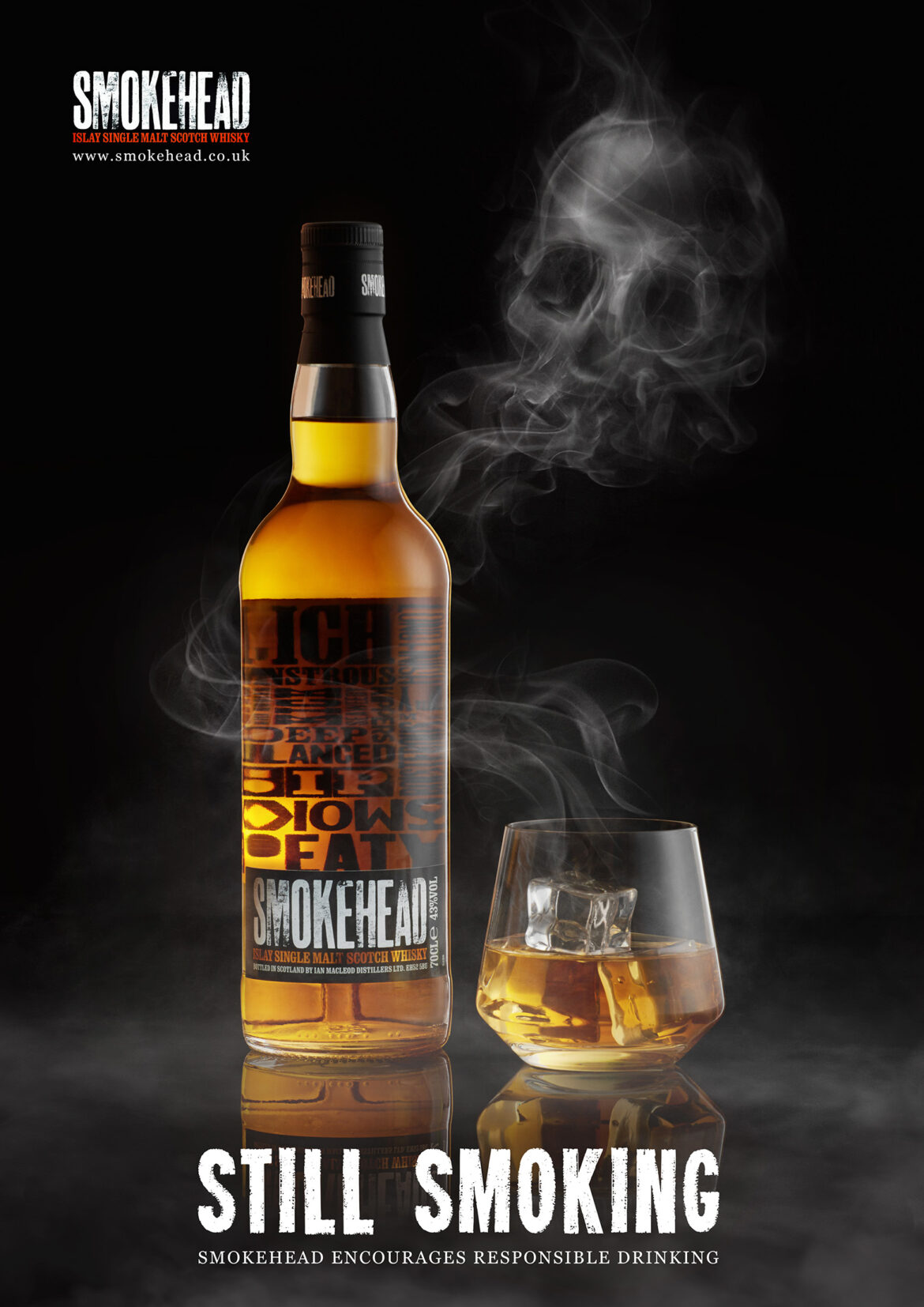 Бутылка виски Smokehead стоит рядом со стаканом, наполненным виски и льдом. Дым клубится вокруг них на темном фоне. Внизу появляется текст STILL SMOKING с призывом к ответственному употреблению алкоголя.